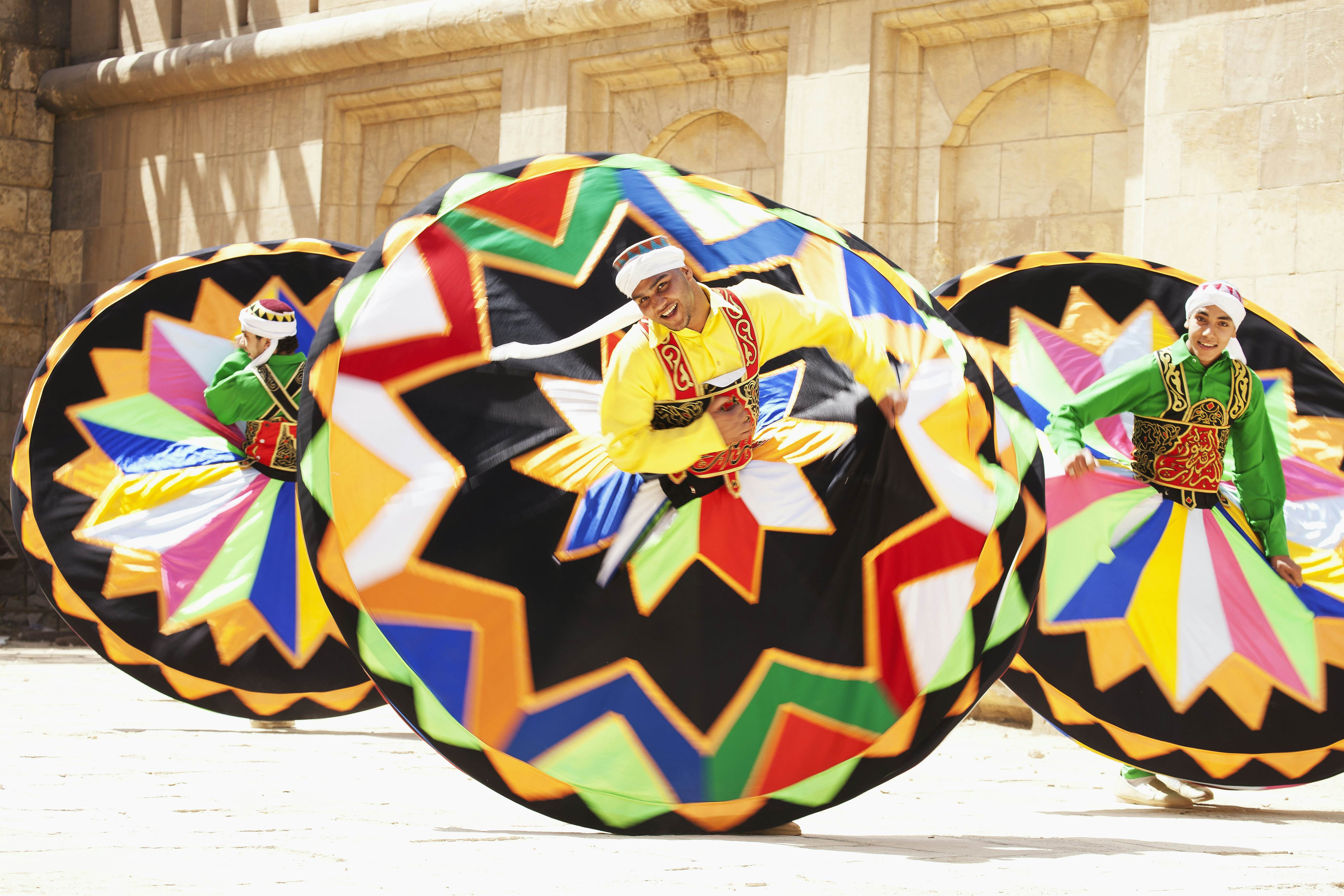 A trio of men twirl in large colorful skirts. 